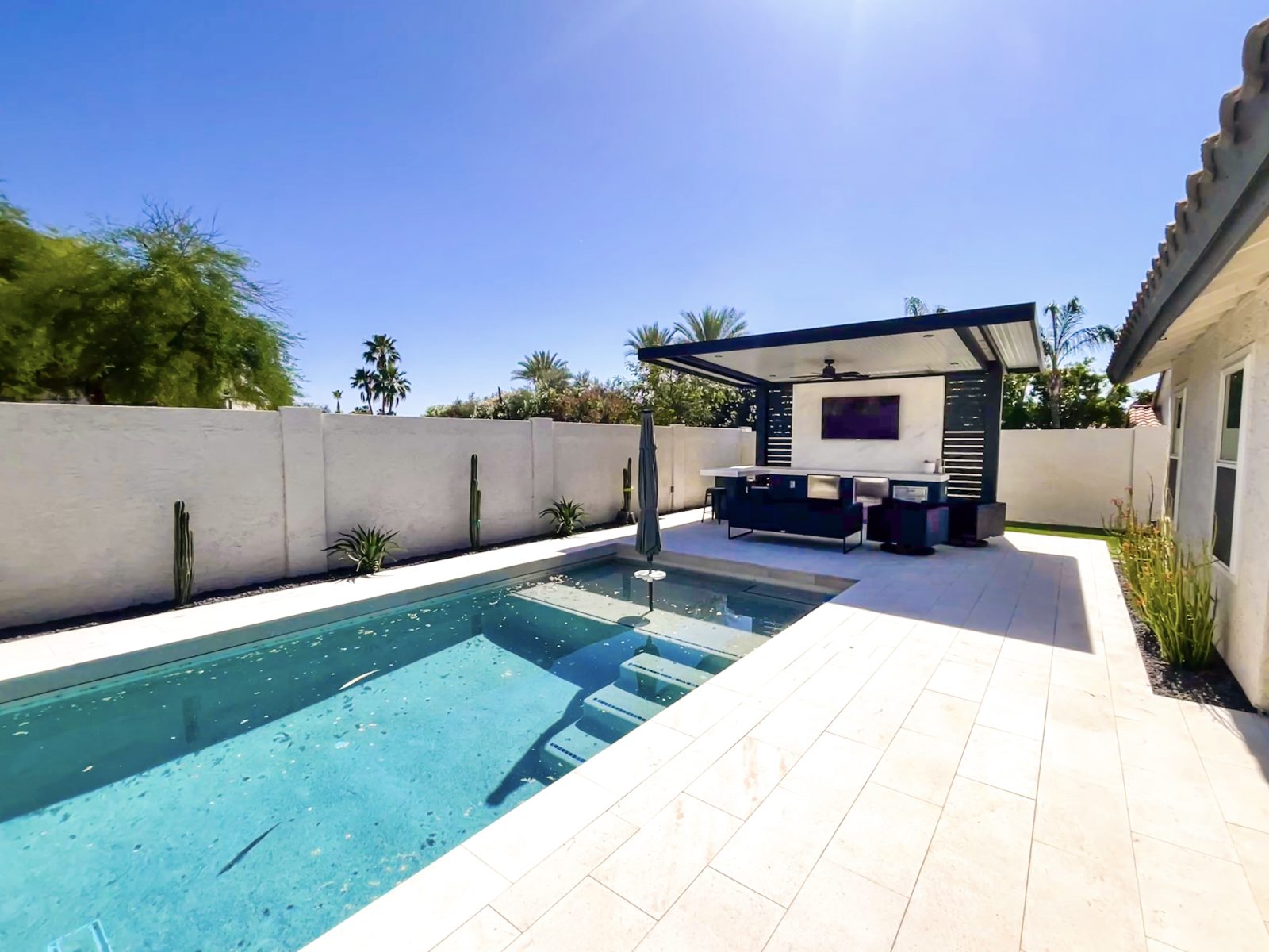 Bright backyard with a rectangular pool, white tiles, and modern outdoor seating under a covered patio area.